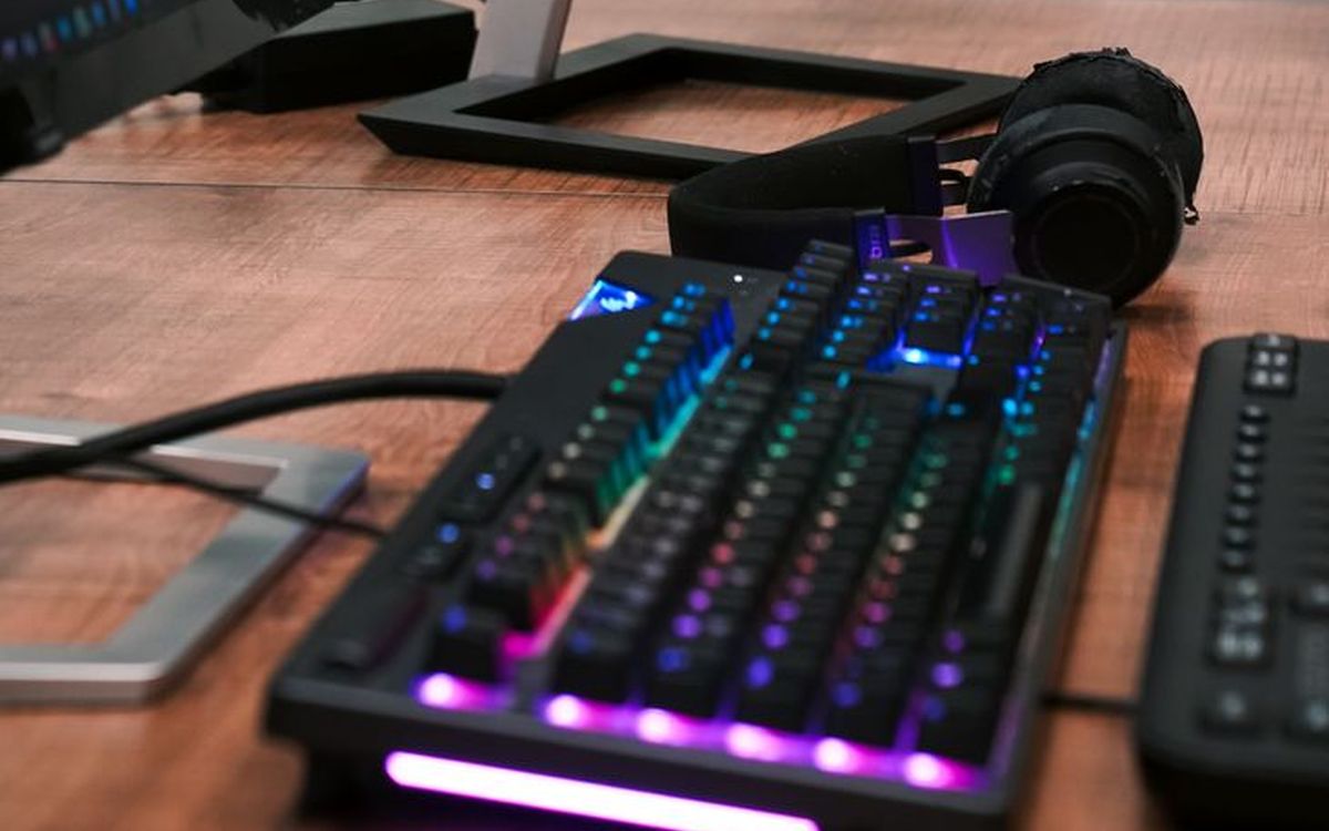Ein modernes Desktop-Setup mit zwei Monitoren, RGB-Tastatur und Kopfhörern auf einem Holztisch.